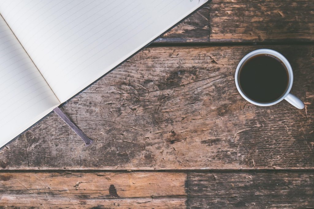 Leeres Journal und eine Tasse Kaffee auf einem Schreibtisch aus dunklem Holz